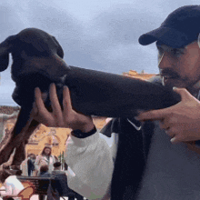 a man in a hat is holding a small black dog in his hands
