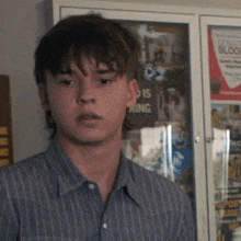 a young man in a striped shirt is standing in front of a glass cabinet with a poster on it .