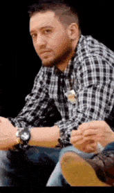 a man wearing a plaid shirt and a watch is sitting down