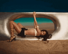 a woman in a bikini is laying in the sand with her arms up