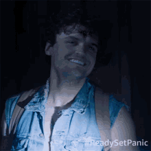 a man in a denim vest is smiling in the dark with #readysetpanic written on the bottom
