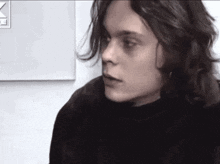 a young man with long hair is wearing a black shirt and looking at the camera .