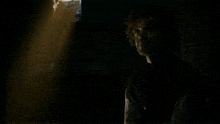 a man with curly hair is standing in a dark room holding a sword .