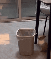 a trash can with a plastic bag on it sits under a table