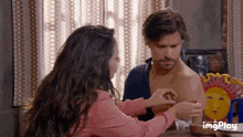 a woman is touching a shirtless man 's arm while sitting at a table .