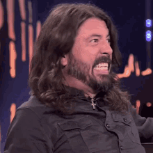 a man with long hair and a beard smiles at the camera