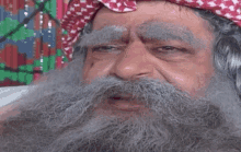 a man with a long beard and mustache is wearing a red and white scarf on his head .