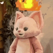 a pink stuffed animal with a fireball on its head is standing in front of a wall .