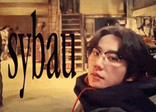 a man wearing glasses stands in front of a sign that says sybaut