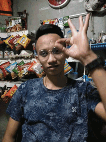 a man wearing glasses is making a funny face in front of a shelf of snacks including a bag of kettle corn
