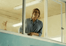 a woman in a blue shirt is smiling while looking out of a window .