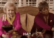 two older women are sitting on a couch smoking cigarettes and drinking wine .