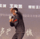 a man in a suit is dancing in front of a screen with chinese writing