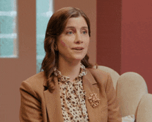 a woman wearing a brown jacket and a brooch is sitting in a chair