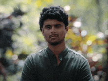 a man in a green shirt looks at the camera with trees in the background