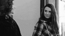 a black and white photo of two women standing next to each other and talking .
