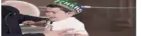 a little boy wearing a hat and tie is crying while being held by a man .