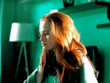 a woman with red hair is standing in a room with a lamp