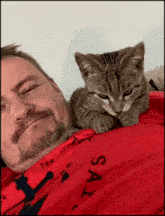 a man with a cat on his shoulder wearing a red shirt that says say