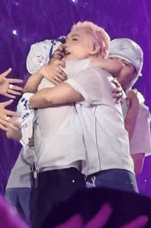 a group of people are hugging each other on a stage in front of a purple background .