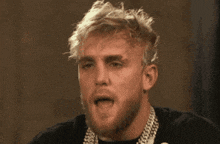 a man with blonde hair and a beard is wearing a black shirt and a chain around his neck .