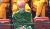a boy with pink hair is sitting in a stadium wearing a green adidas jacket