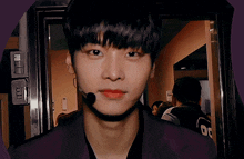 a young man with a microphone in his mouth is standing in front of a door and looking at the camera