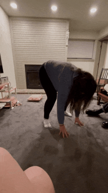 a woman in a blue sweater and black pants is bending over on the floor