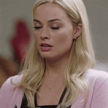 a woman with blonde hair wearing a pink cardigan and a cross necklace