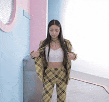 a woman wearing plaid pants and a white top is standing in a hallway