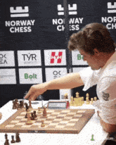 a man is playing chess in front of a sign that says " norway chess "