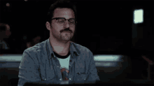 a man wearing glasses and a mustache is sitting at a table