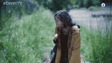 a woman in a yellow jacket is standing in a field with the words #crypttv behind her