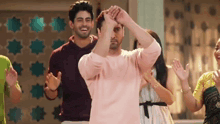 a man in a pink shirt is dancing with his hands in the air