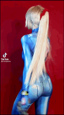 a woman with long blonde hair is wearing a blue jumpsuit with a red bow in her hair .