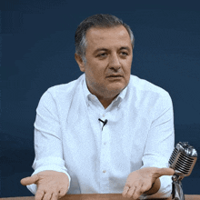 a man in a white shirt is sitting at a table with a microphone in front of him