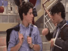two young men are standing next to each other in a room and talking to each other .