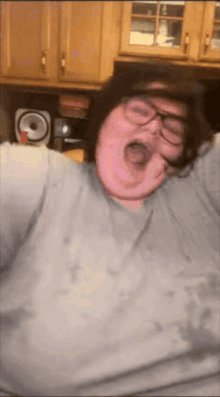 a man wearing glasses and a gray shirt is yawning