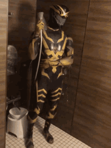 a man in a black and gold superhero costume is holding a hose in a bathroom