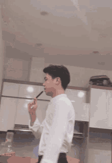 a man in a white shirt is smoking an electronic cigarette in a kitchen .