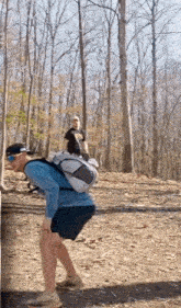 a man with a backpack is standing on a dirt road in the woods .