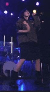 a person singing into a microphone with a drummer in the background