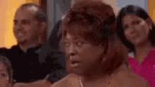a group of people are sitting in a room with a woman making a surprised face .