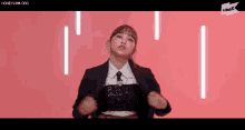 a woman in a suit and tie is standing with her hands on her hips in front of a pink background