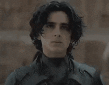a young man in a black suit is holding a sword in his hand .