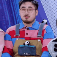 a man with a beard and glasses is wearing overalls and a striped shirt with a panda on it .
