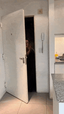 a woman peeking out from behind a door with a phone on the wall above it