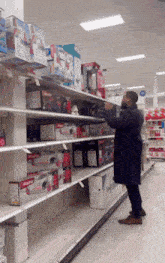 a man in a black coat is standing in front of a shelf that has a red box that says ' barbie '