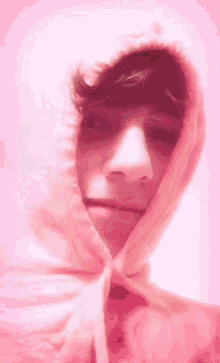 a young man is wearing a pink hoodie and making a funny face .