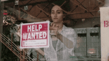 a woman is holding up a help wanted sign in a window